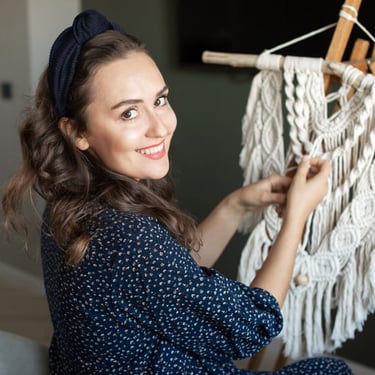 Mujer de espaldas, sonriendo mientras teje macrame blanco