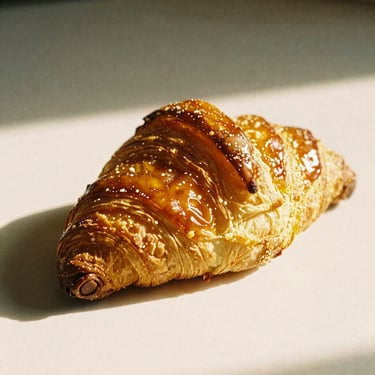 A pain au chocolat with glossy, crisp laminated layers, chocolate batons visible at the ends, warm editorial photography, 35mm film