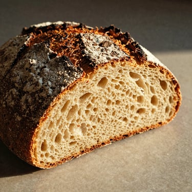 A rustic loaf of Tourte de Meule, thick dark crust, dusted with flour, sliced to reveal wide open crumb, warm side light, warm editorial photography, 35mm film