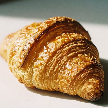 Close-up of a classic French croissant, golden flaky layers perfectly defined, warm morning light highlighting the pastry, warm editorial photography, 35mm film