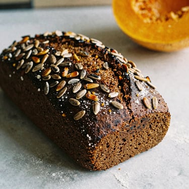 A dark, dense rye bread loaf, loaded with toasted pumpkin and sunflower seeds, rustic kitchen setting, warm editorial photography, 35mm film