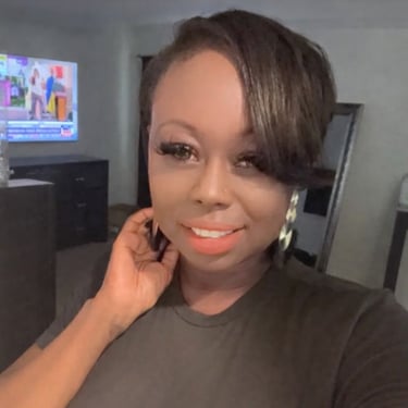 Smiling woman with short side-swept hair, false eyelashes, and hoop earrings in a modern living room.
