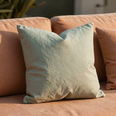 Hands arranging a weather-resistant textured throw pillow on a high-end outdoor sofa, warm golden-hour sunlight, close-up editorial shot.