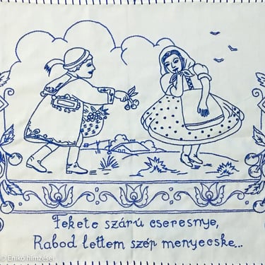 Kék fonallal hímzett falvédő részlet két alakkal és szöveggel.