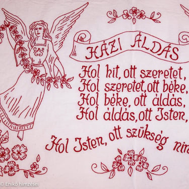 Házi áldás falvédő részlet piros fonallal hímzett szöveggel és angyallal.