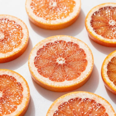 Macro close-up of glistening sliced grapefruit and blood orange on a clean white surface, vibrant citrus tones, bright direct morning sunlight with soft shadows, crisp focus, high-end editorial food photography.
