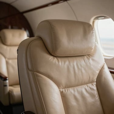 Macro detail of hand-stitched champagne leather seating inside a Gulfstream cabin, natural low-key side lighting.