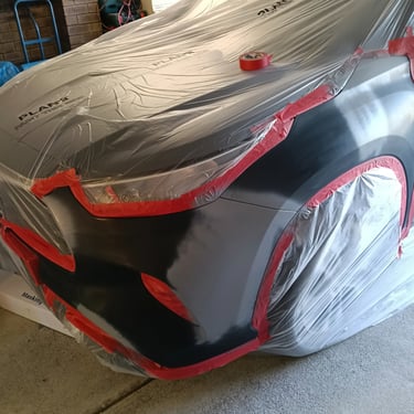 Professional car body repair with plastic masking and red tape for automotive painting.