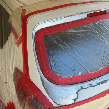 White car rear window masked with red tape and plastic film for automotive body paint repair.