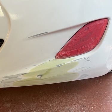 White car bumper repair showing sanded body filler and masked reflector for auto paint prep.