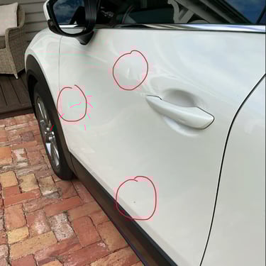 Close-up of small dents and door dings on a white car door circled in red for auto body repair.