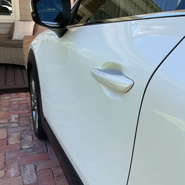 Close-up of a white SUV car door with a sleek handle parked on a driveway following dent repair.