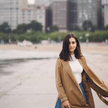 Mujer viste elegante gabardina y jeans en la playa y de fondo la ciudad moda internacional México