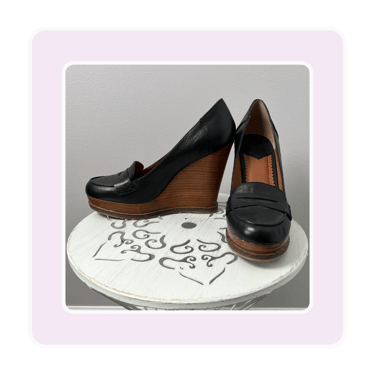 Pair of black leather platform wedge loafers for women displayed on a white decorative stool.