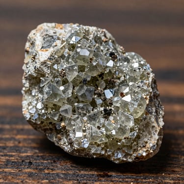 Macro shot of raw gray-olive zeolite mineral granules resting on a dark rustic wooden surface, sharp focus on crystalline geological textures, bright natural daylight.