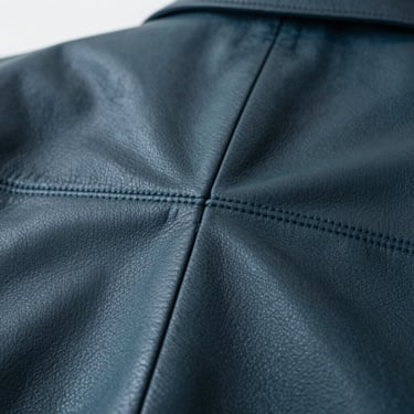 Macro shot of heavy leather jacket seams being stitched with absolute precision, dark elegant tones