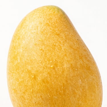 Macro shot of a golden ripe Alphonso mango, smooth skin, vibrant tropical color, clean white background, studio lighting, commercial photography