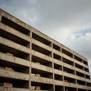 Wide cinematic 2.39:1 framing of a brutalist concrete building under heavy overcast sky, dramatic shadows