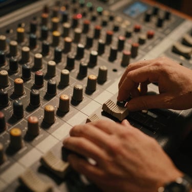 Extreme close-up of hands adjusting an analog sound board in a dim studio, warm tungsten light