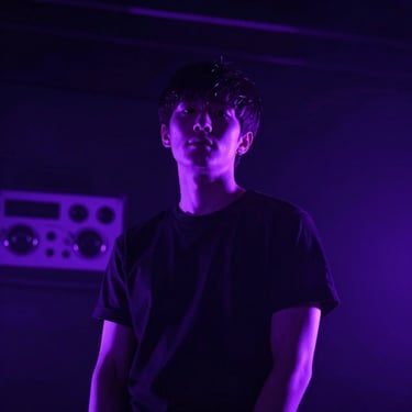 Low-angle portrait of a synthwave artist with neon violet lighting, dramatic shadows, analog gear in background, square aspect.