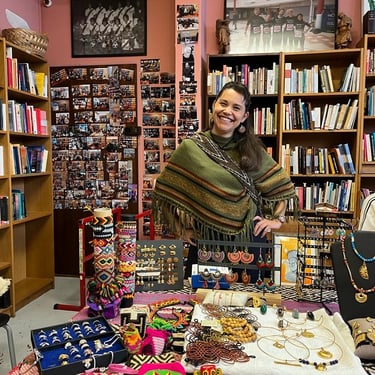 Femme souriante portant un poncho, debout dans une librairie remplie de bijoux artisanaux faits main