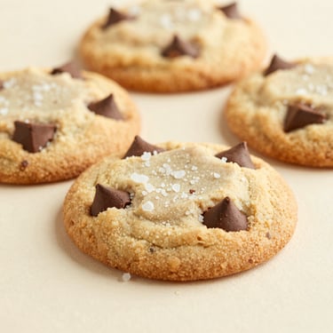 Macro shot of thick, textured chocolate chip cookies, sea salt flakes on top, soft warm shadows