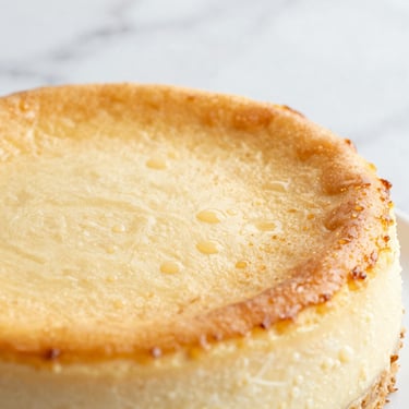 Close-up of a baked vanilla bean cheesecake, golden caramelized top, condensation droplets, marble background