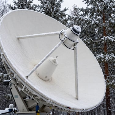 Extreme close-up of a ruggedized satellite dish active in a heavy blizzard, thick ice melting off the heated transmitter arm, dark pine forest background