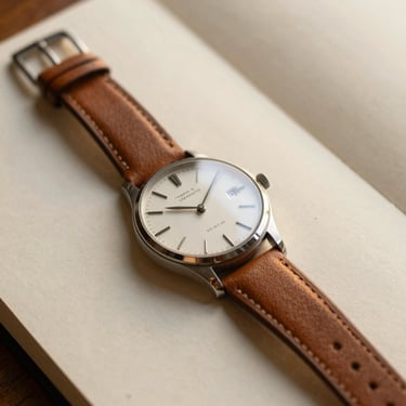 Close-up of a classic mechanical watch on a leather strap resting on a textured paper journal, warm golden hour light