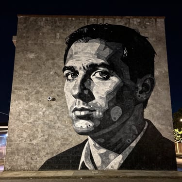 High-contrast photo of a massive outdoor mural on a concrete brick wall, dramatic night lighting, intense graphic style.