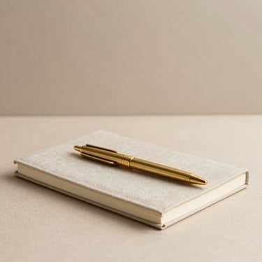 Sleek brass pen resting on a heavy linen notebook, warm neutral background, soft shadows
