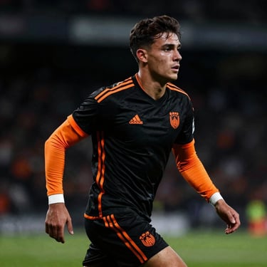 Heroic portrait of a young professional football player in black and orange kit, dark stadium background, dramatic side light