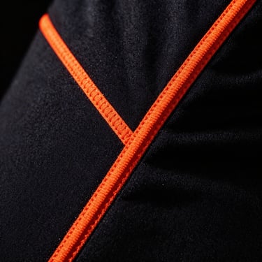 Macro detail of heavy cotton technical hoodie seams, neon orange stitching on deep black fabric, dramatic side lighting, high-contrast.