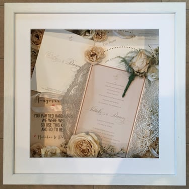 a photo of a memory box full of wedding items and preserved wedding bouquet flowers in a deep frame