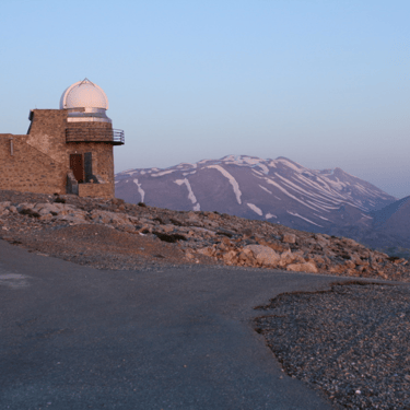 Skinakas Observatory in Crete with snow-capped mountains in the backdrop