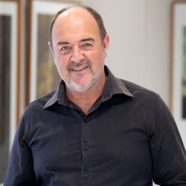 Portrait of Martin Osner, South African photographic artist and painter, smiling in a fine art gallery setting
