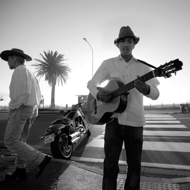 Street guitarist performing near a seaside crossing in Camps Bay, photographed in black-and-white fine art detail.