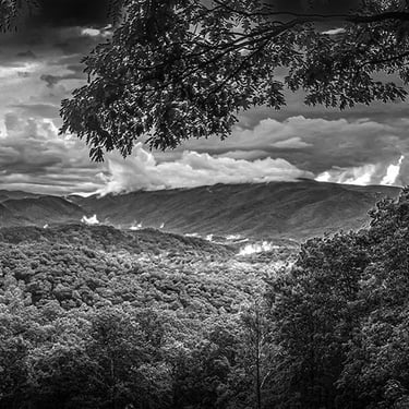 Dramatic early morning clouds swirl around the rugged peaks of the Smoky Mountains, hanging over the forested landscape