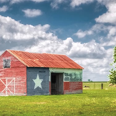 Rustic barn painted with Texas state flag motif, showcasing Texas pride in a rural Texas countryside setting