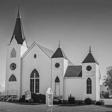 Black and white photo of a small white country church in rural Texas with traditional steeple and open sky