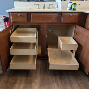 A bathroom vanity has three levels of pull out shelves on one side of the cabinet and a single with riser on the other side.