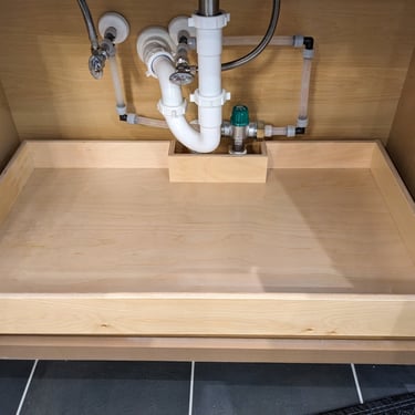 A roll out cabinet shelf that is custom built to fit around plumbing obstacles beneath a sink.