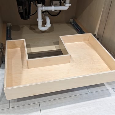 An empty roll out shelf underneath a kitchen sink.
