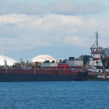 A stern view of tugboat Albert pushing barge Margaret past an industrial facility.