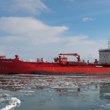 Left side view of tanker ship Algoluna on icy water, with a blue sky and sun reflecting off the side of the hull.