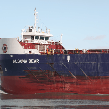 Freighter Algoma Bear's bow pushing water, passing a red navigation buoy.