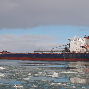 Port side stern view of freighter Algoma Bear on icy water with a plume of steam coming out of her funnel.