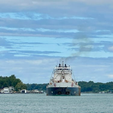 Front view of Great Lakes freighter Algoma Buffalo with trees in the background and a blue sky with streaks of clouds.