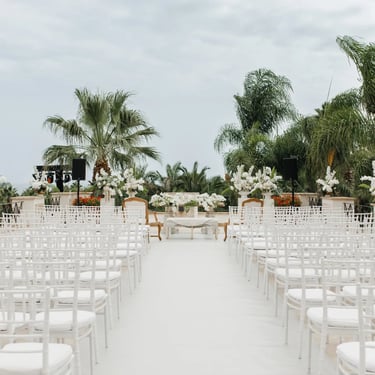 Outdoor ceremony setup with white chairs and palms