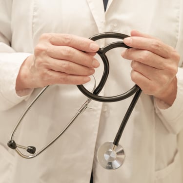 Close-up of a healthcare professional in a white lab coat holding a black medical stethoscope.